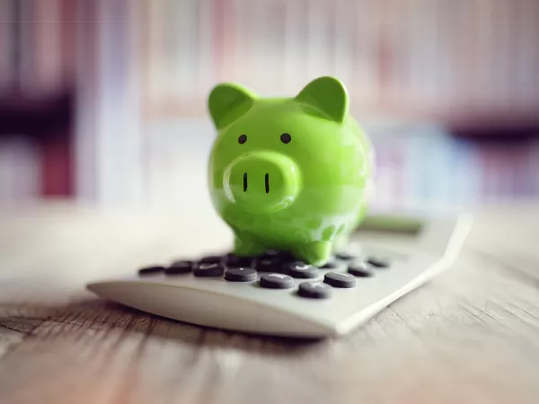 A green piggy bank sitting on a calculator.