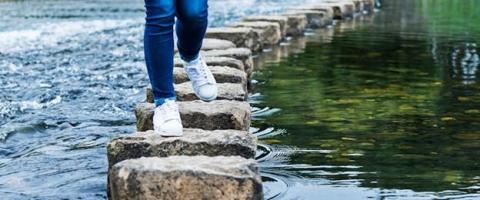 person walking across steppingstones in a river