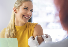 Smiling woman being applied a band aid in her left arm