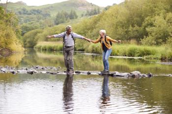 Older couple walking on stones across water.