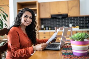 Woman sitting at computer, holding documents